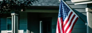 American Flag hanging off of a house porch outside.